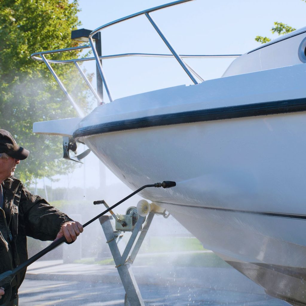 man cleaning a boat hull with a power washer