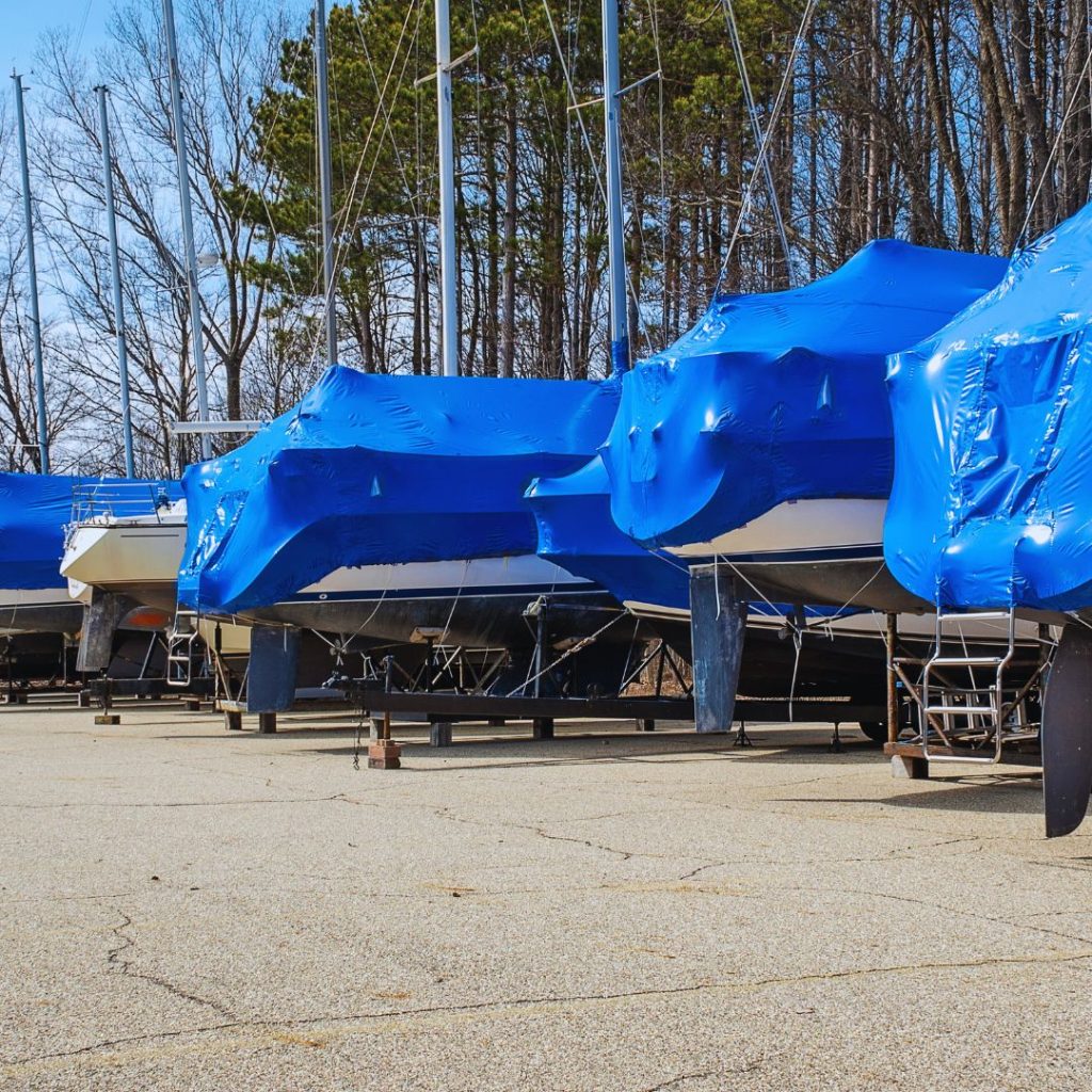 boats with blue covers stored on a lot with their trailers